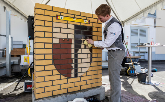 Pierre Holze, Maurerweltmeister bei den WorldSkills 2022, errichtet eine Mauer mit Annweilerer Wappen inklusive Wasserwaage und steht den Auszubildenden Rede und Antwort.